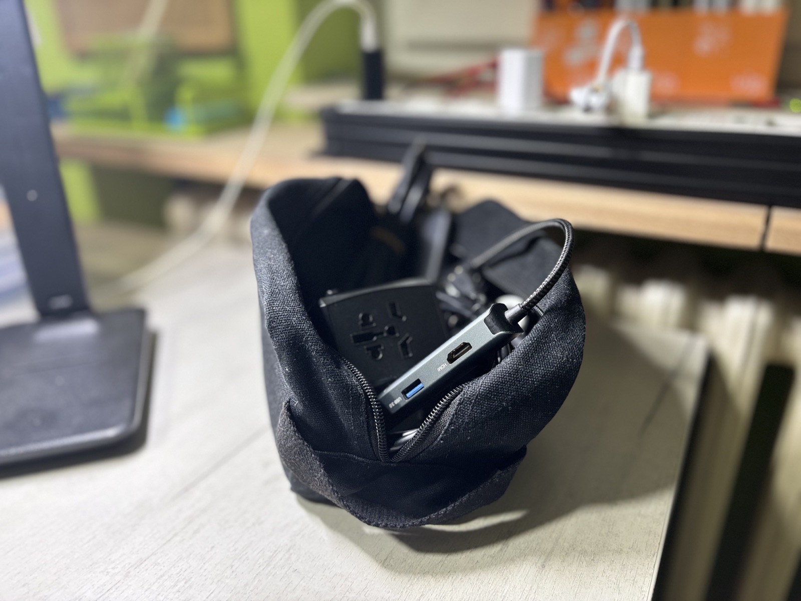 Open black canvas cable bag containing a USB-C hub, power adapter, and coiled cables on a desk